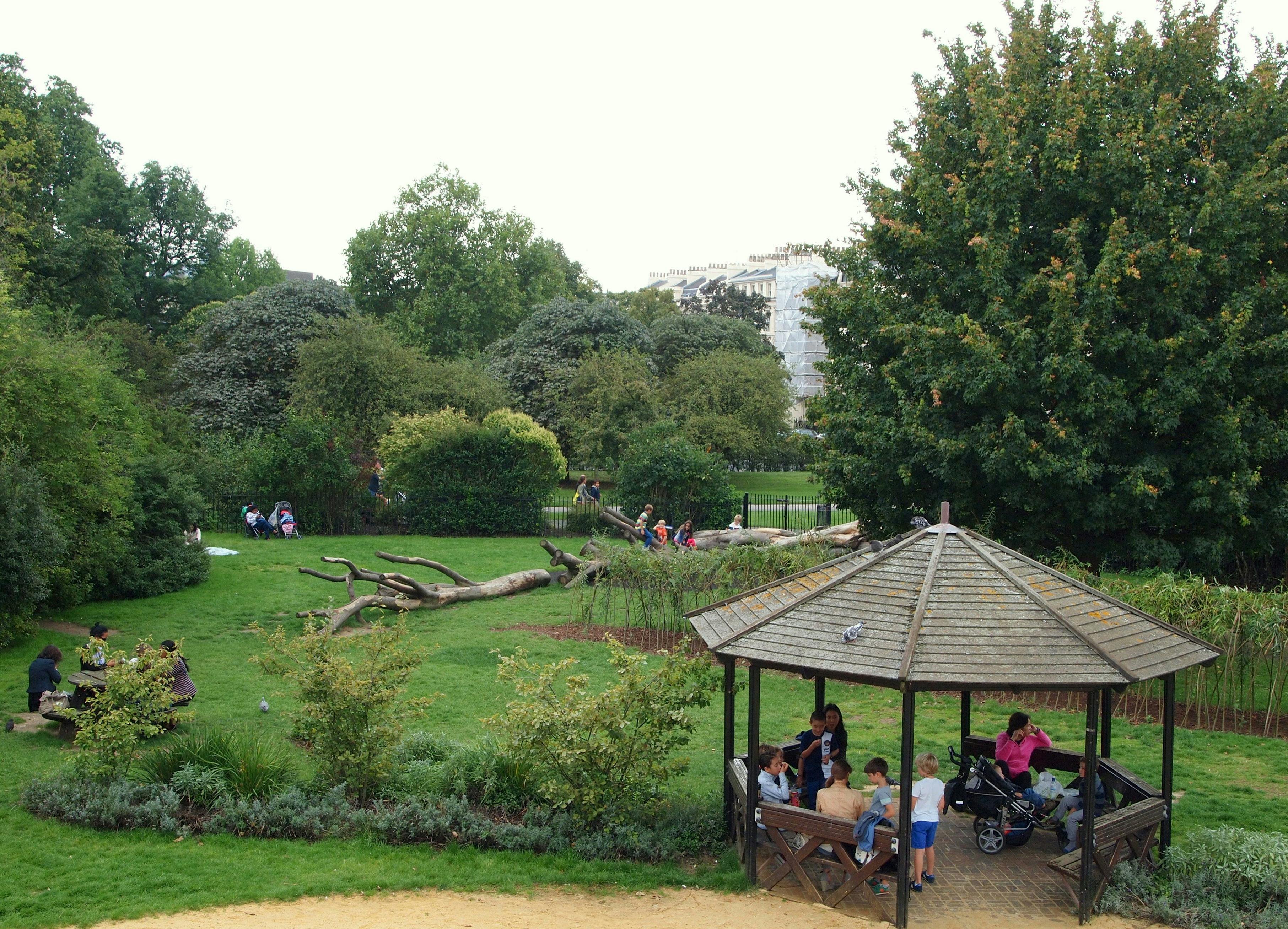 녹지와 건물을 배경으로 정자에 앉아 있는 사람들, 벤치에 앉아 있는 사람들, 쓰러진 나무 근처의 공원 풍경.