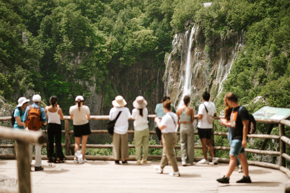 A group of people stand on a viewing platform overlooking a waterfall surrounded by lush greenery.