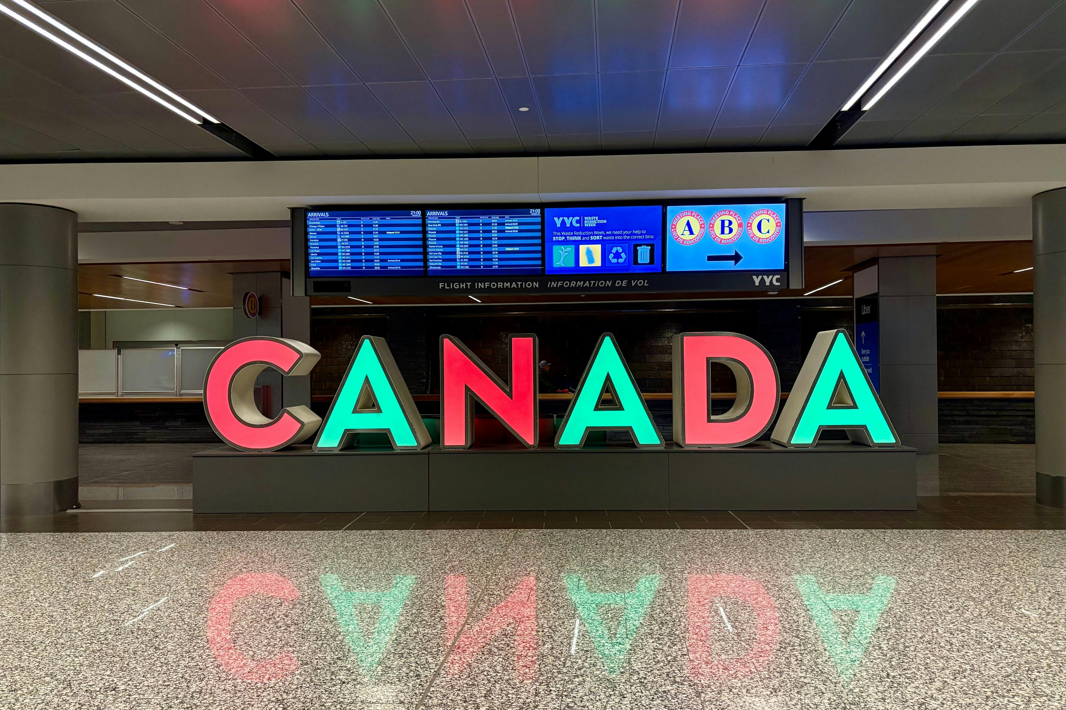 机场内大型彩色“加拿大”字母，背景为航班信息屏幕。
