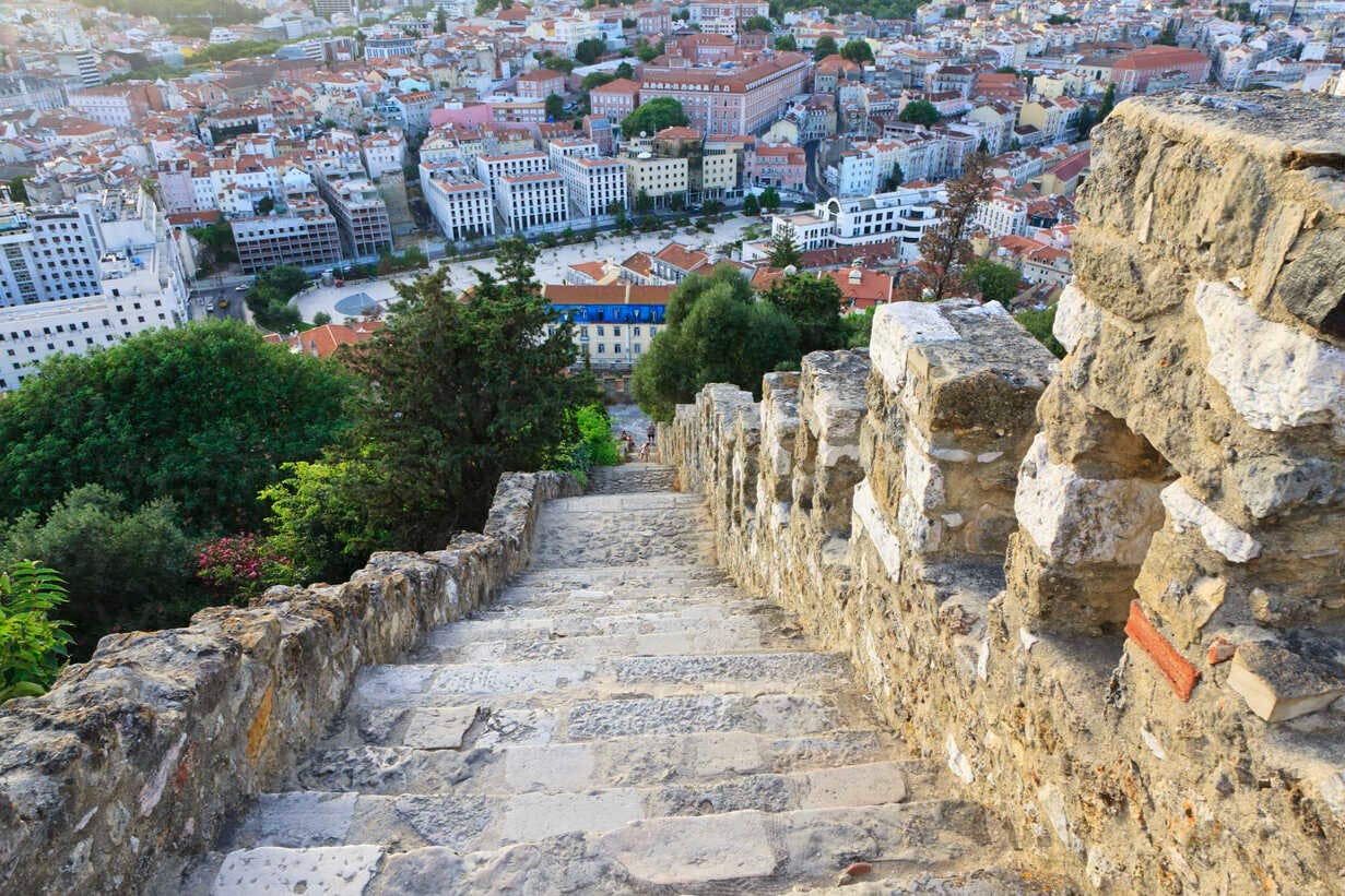 Steep stone steps descending from a high vantage point, overlooking a densely built town with trees and various buildings.