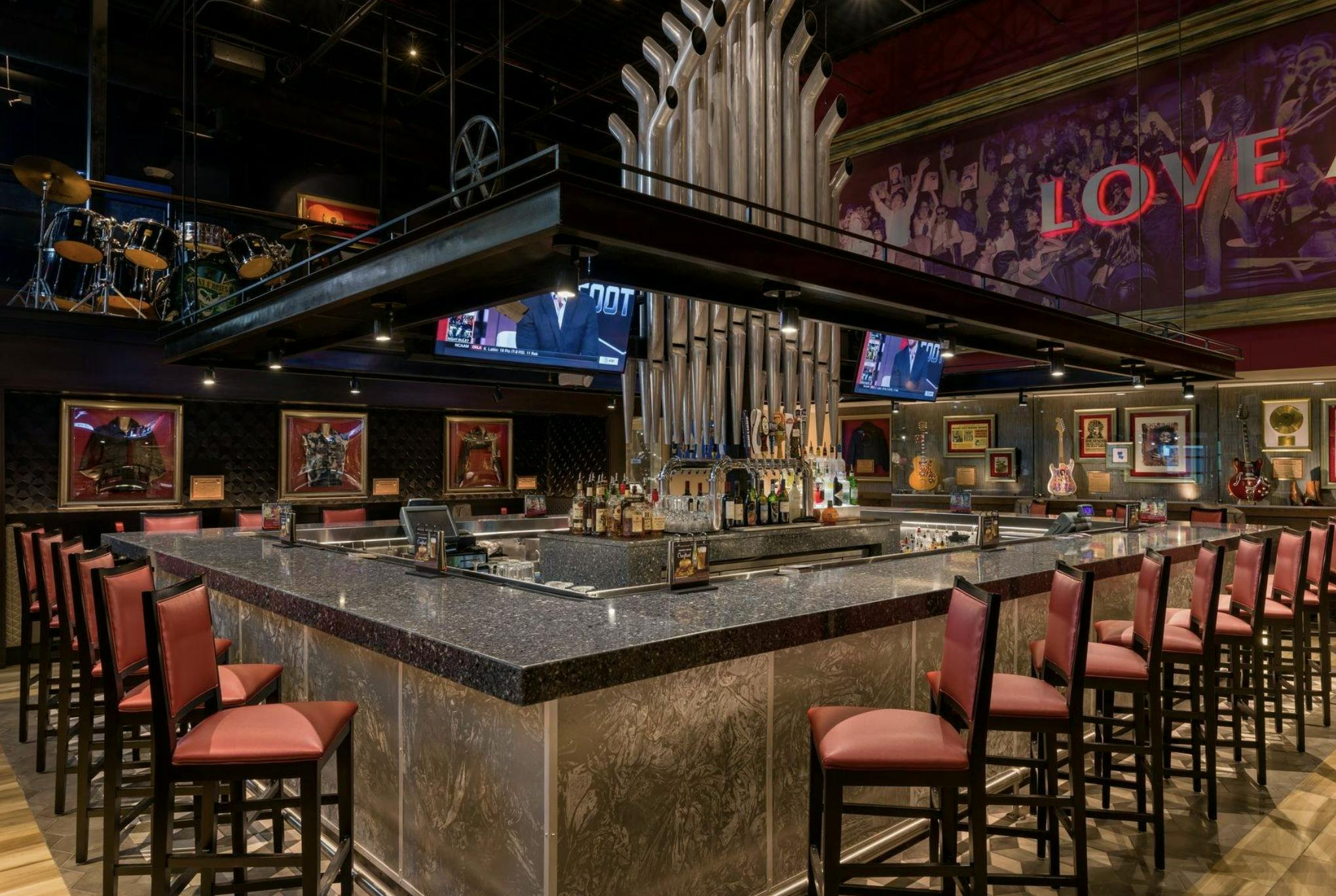 Modern bar with high chairs, a variety of bottles displayed at the counter, and multiple TV screens showing sports.