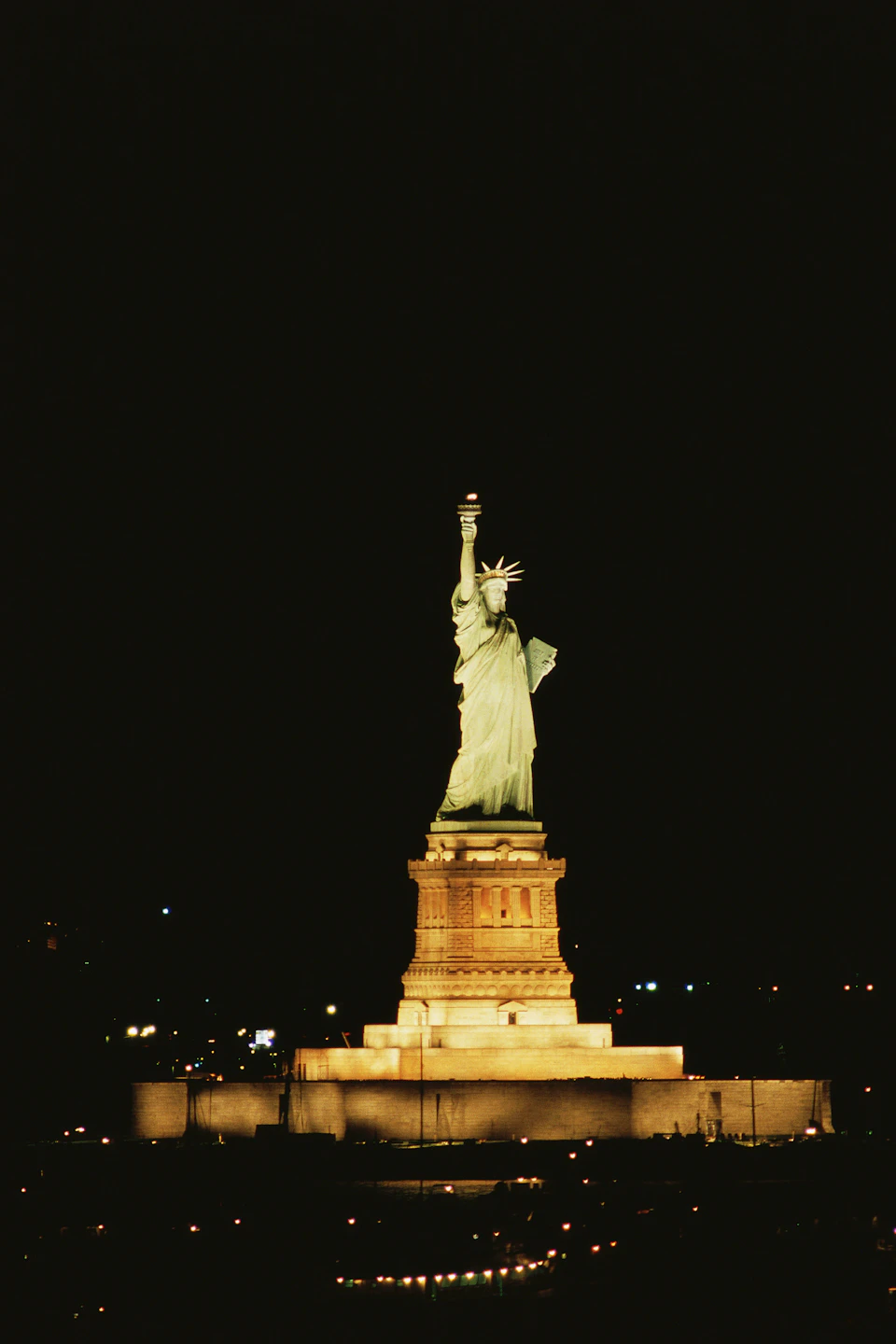 The Statue of Liberty illuminated at night with a dark sky in the background.