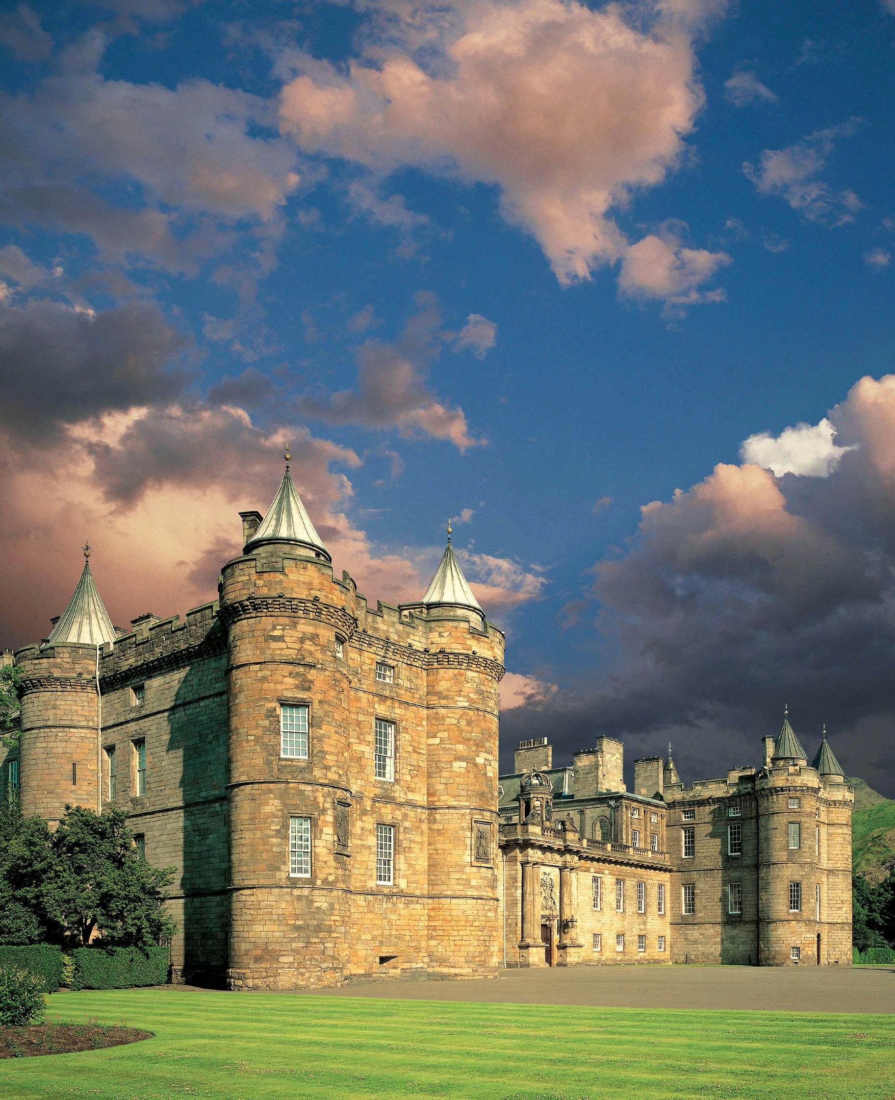 Castello con torrette coniche sotto un cielo drammatico con nuvole rosa e blu. Sono visibili i muri di pietra e la vegetazione lussureggiante.
