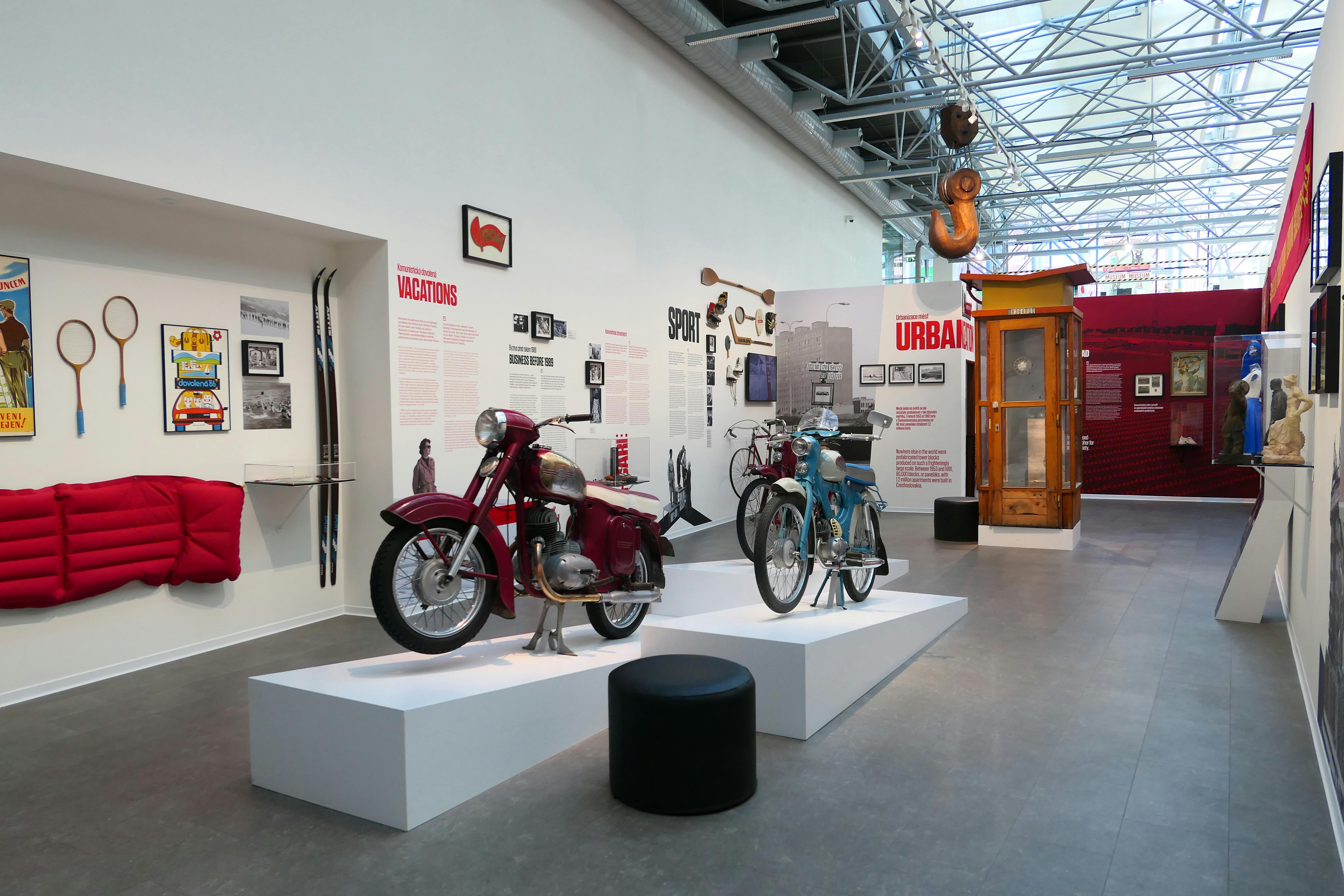 博物馆展览包括白色平台上的老式摩托车、黄色电话亭和带有文字和照片的墙壁展示。