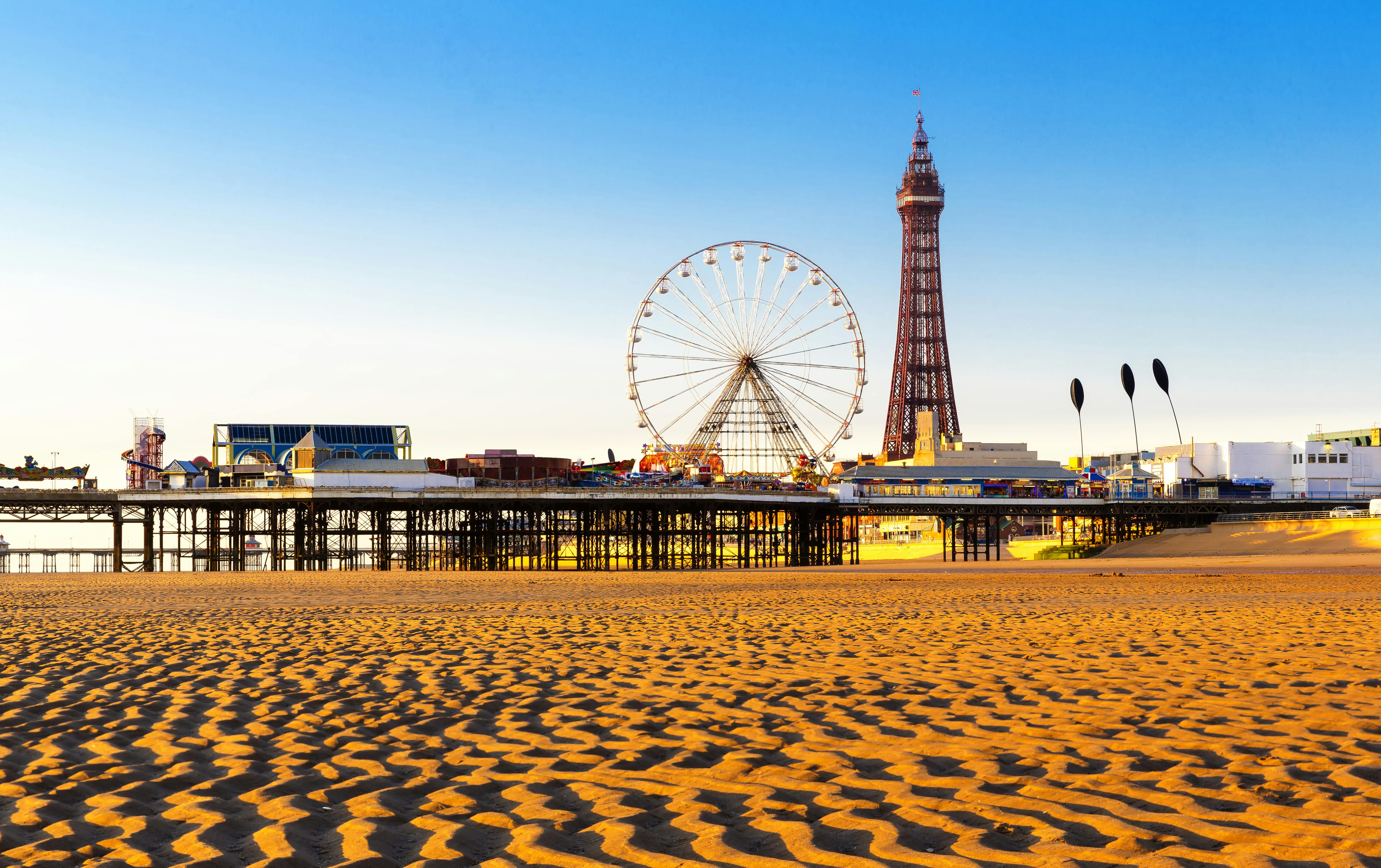 A sandy beach with a Ferris wheel and an Eiffel Tower-like structure on a pier, against a clear blue sky.
