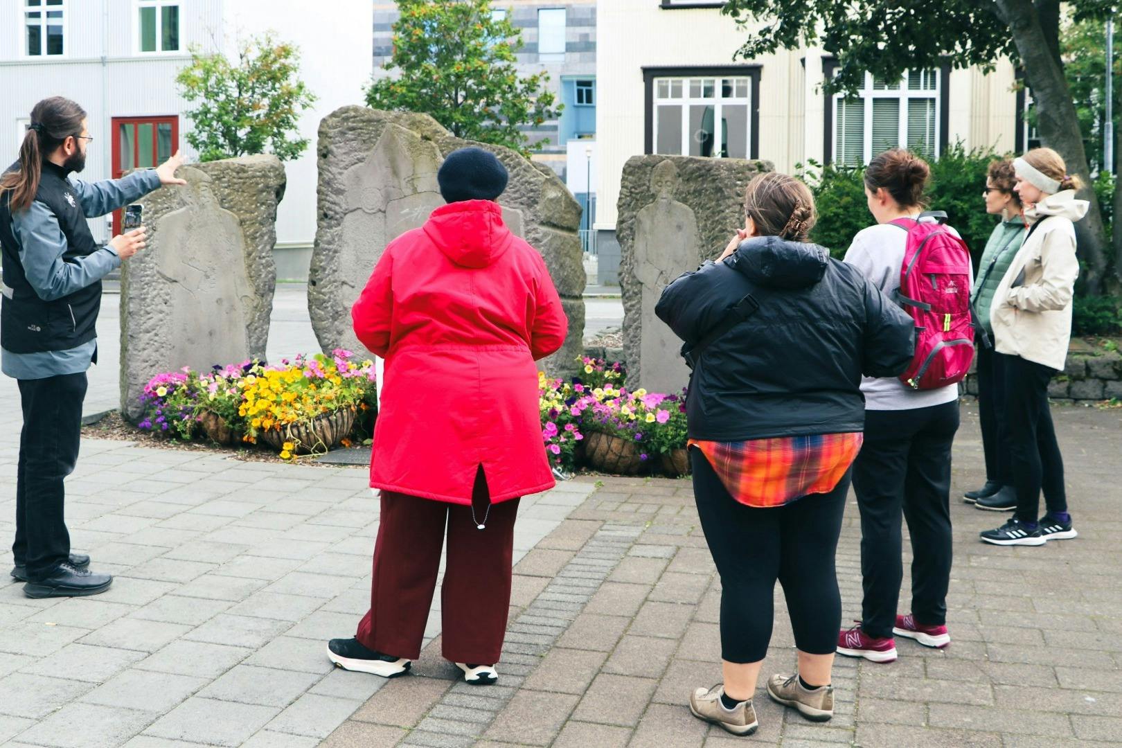 세 사람이 꽃과 보도로 둘러싸인 도심 속 전광판으로 배치된 커다란 석판을 마주하고 서 있습니다.