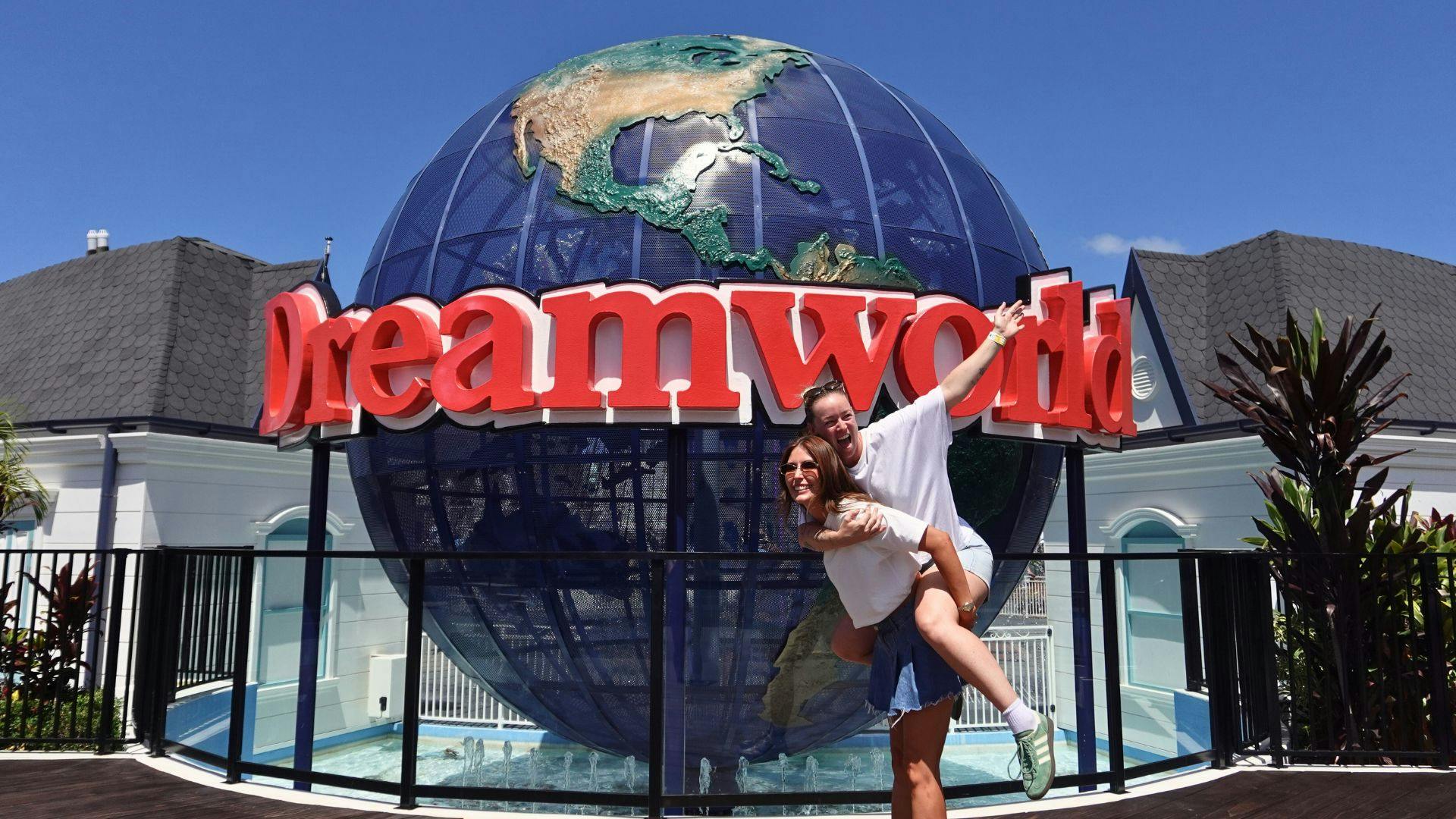 Two people posing playfully in front of a large globe sculpture with the word 'Dreamworld' in bold red letters.