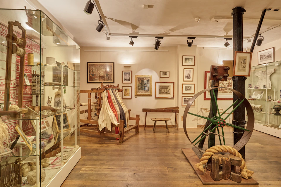 A museum room featuring framed artwork, display cabinets, nautical ropes, and a wooden wheel on a stand.