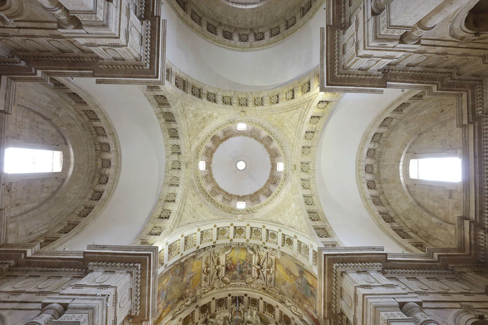 Ornate cathedral ceiling with a central dome, painted frescoes, and architectural details in a grand, symmetrical design.