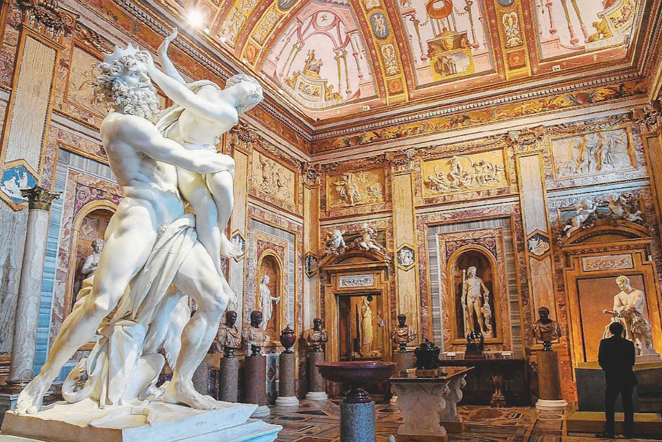 An ornate room in a museum featuring a marble sculpture in the foreground, surrounded by intricate decorations and statues.