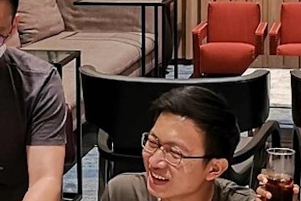 Three people gathered around a table with laptops, coffee, and pastries, smiling and talking in a cozy indoor setting.