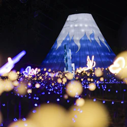 A bright blue and white illuminated tent-like structure surrounded by glowing blue and yellow lights at night.