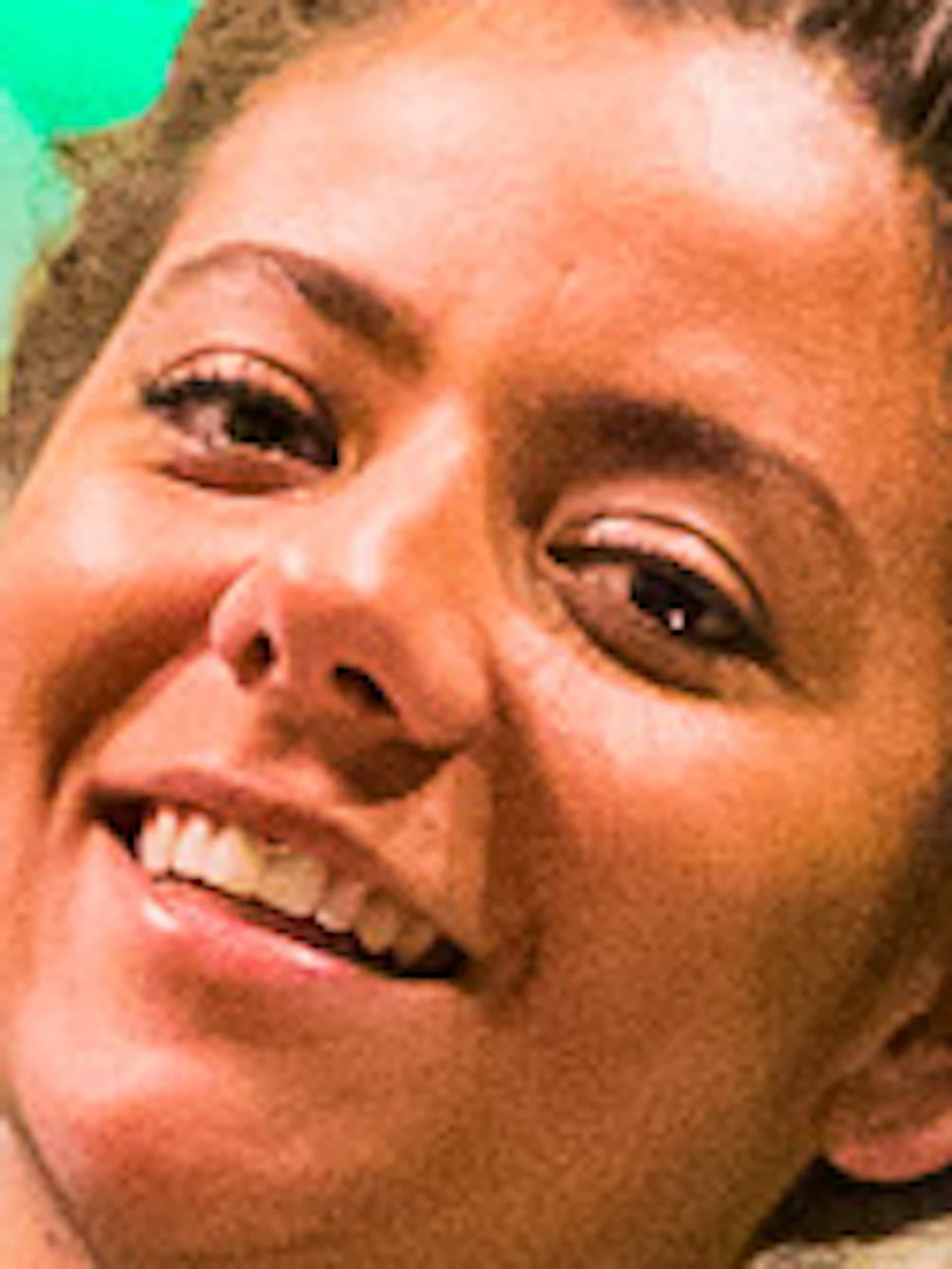 Smiling bartender in a dark shirt and green bow tie holds up a glass of beer. "WE SAY PROOST!" is illuminated on the wall behind her.