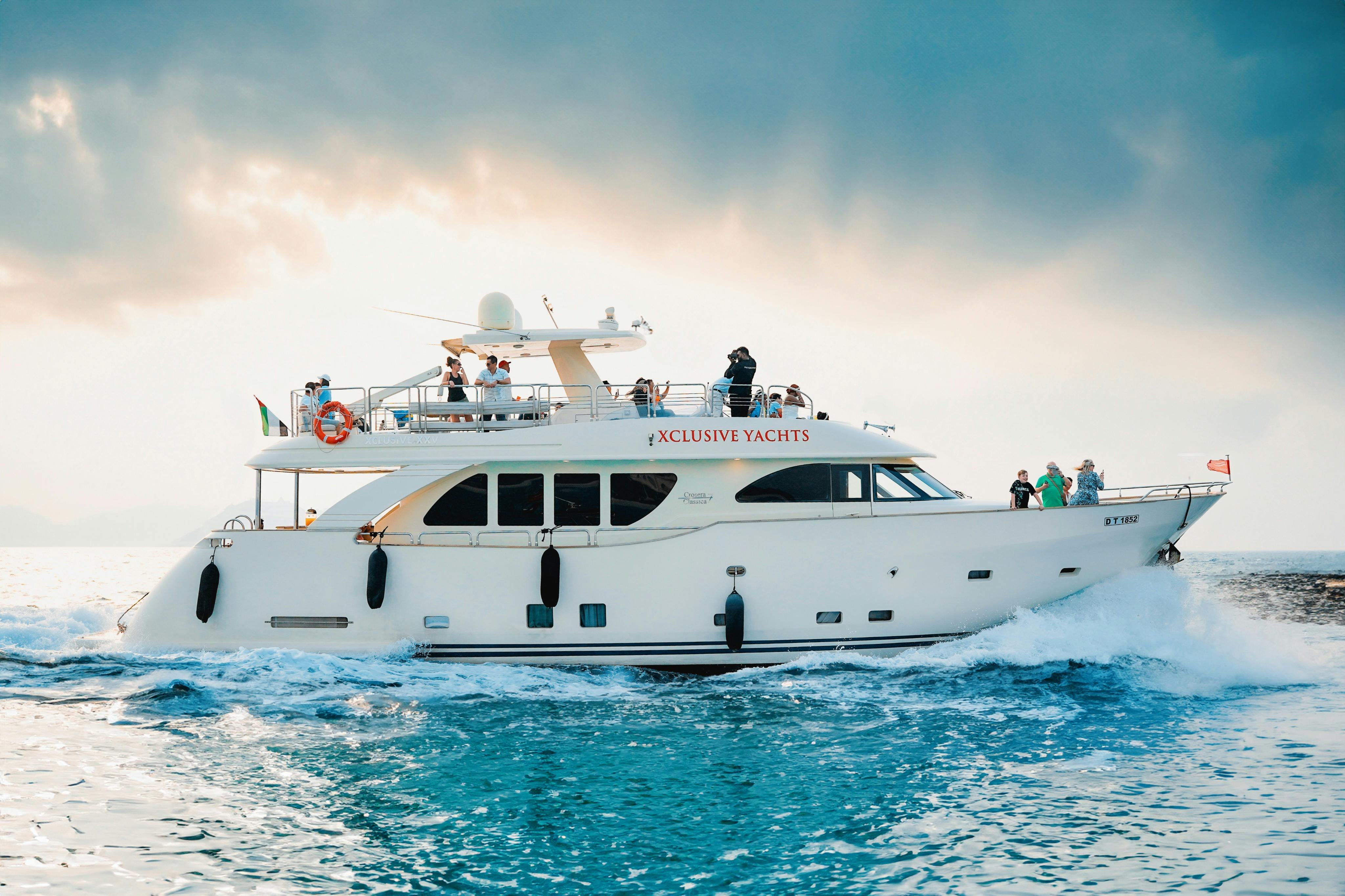 「エクスクルーシブヨット」と名付けられた豪華なヨットは、青い海を航海しています。一部曇り空の下で数人が乗船しています。