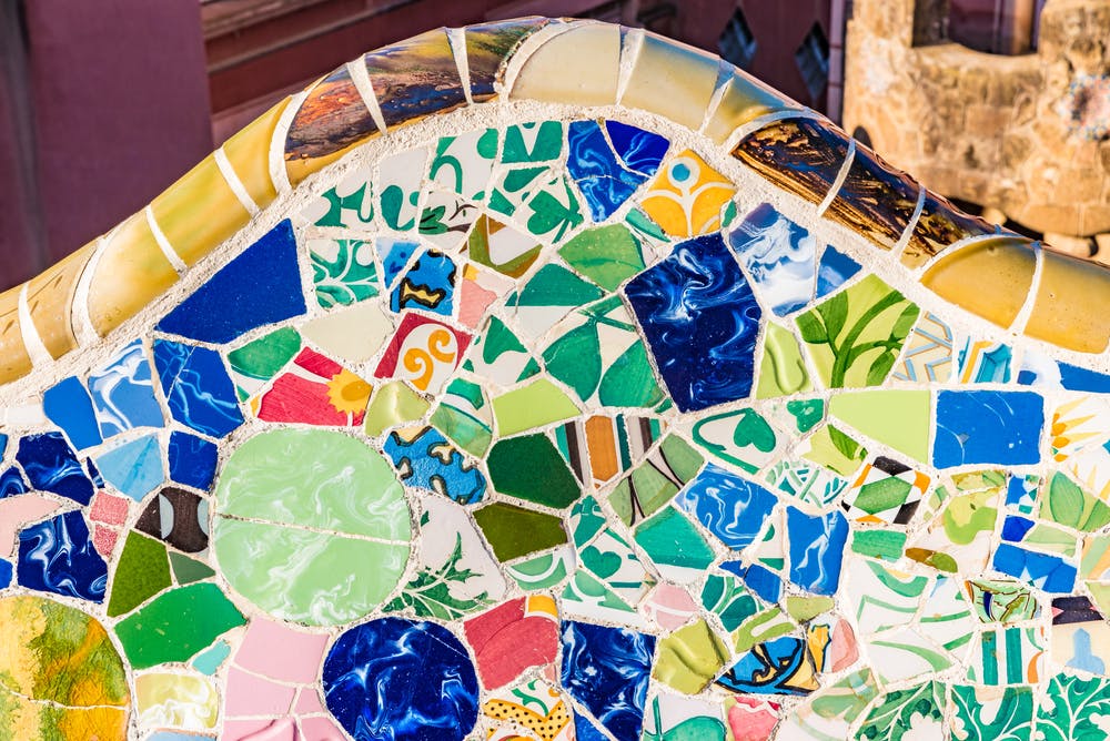 Primo piano di un colorato mosaico di piastrelle di varie forme, colori e texture con un bordo curvo nella parte superiore.