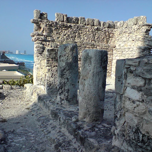 Alte Steinruinen mit hohen Säulen, die moderne Gebäude und das Meer im Hintergrund überragen.