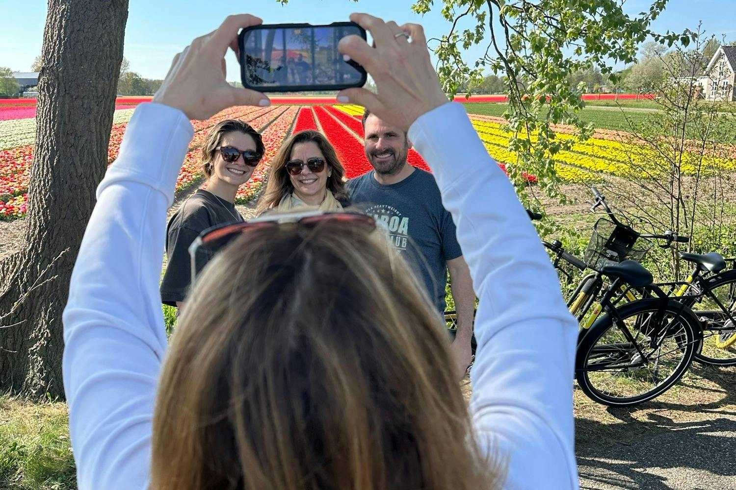 一个人拍摄了三个微笑的人站在五颜六色的花田前的照片。 背景为树和树枝。