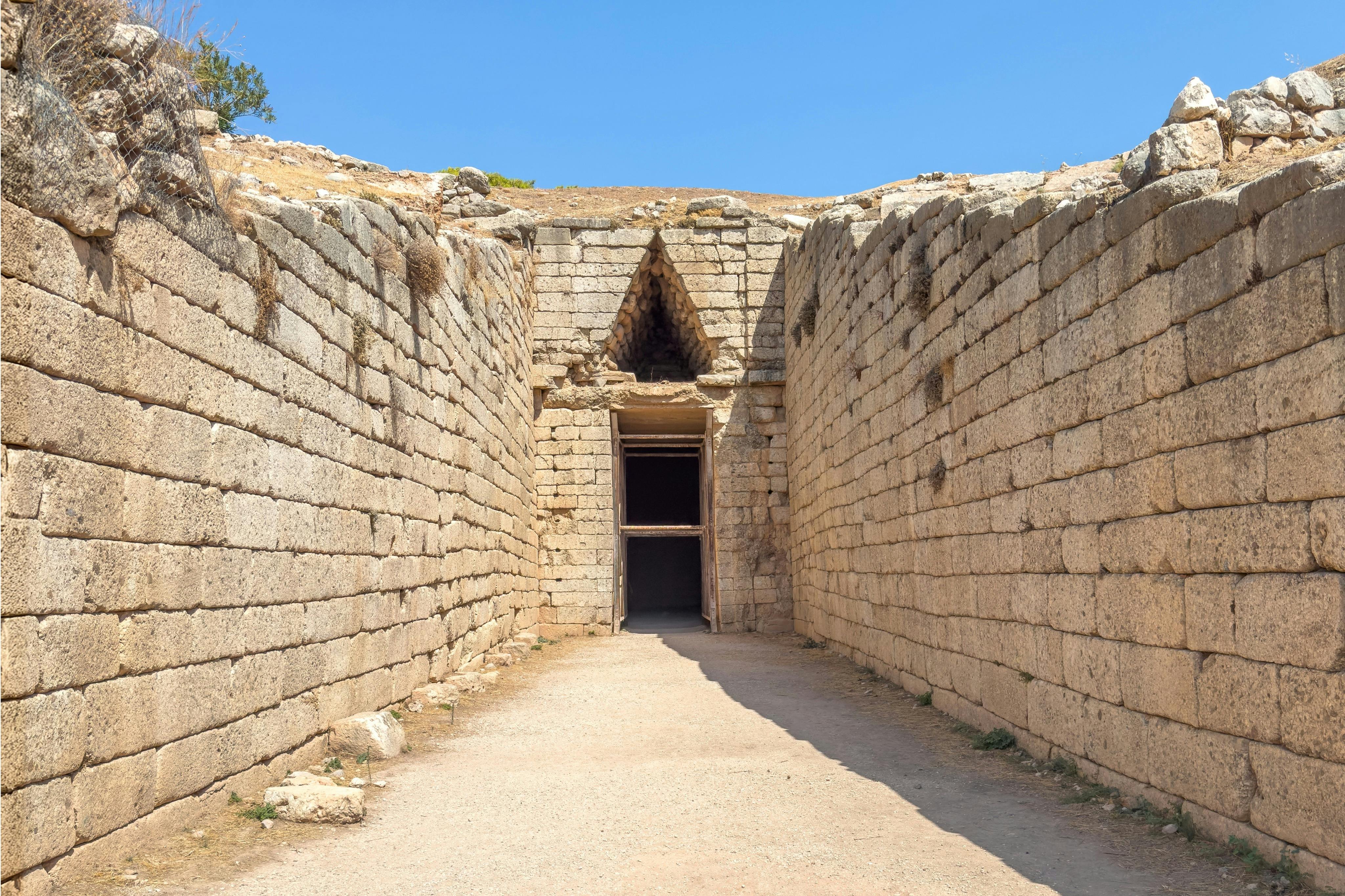 맑고 푸른 하늘 아래 출입구 위에 삼각형의 입구가 있는 고대 건축물로 들어가는 돌로 둘러싸인 입구.