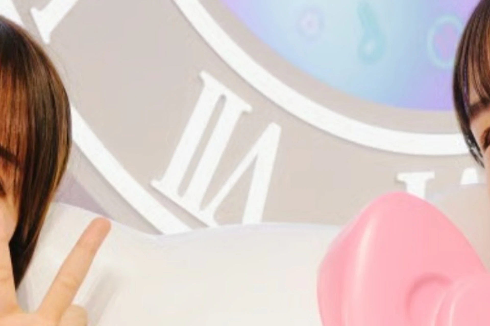 Two people posing with a Hello Kitty statue in a colorful setting with a clock-themed backdrop.