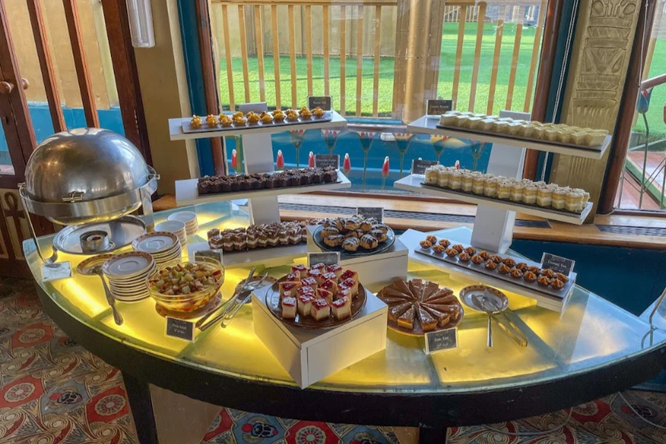 A dessert buffet with various cakes, pastries, and desserts displayed on a lit table in a brightly lit room.