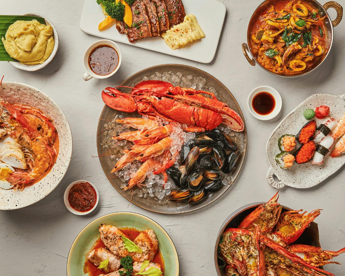 A table spread of various dishes, featuring a central plate of seafood including lobster, shrimp, and mussels on ice.