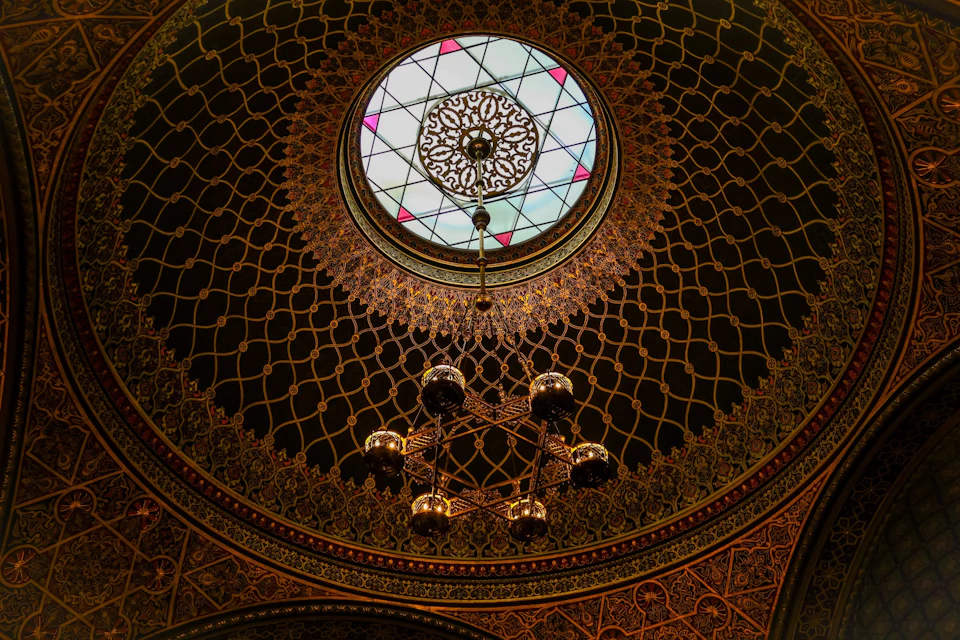 A detailed dome ceiling with intricate patterns, a central stained glass circle, and a decorative chandelier hanging below.
