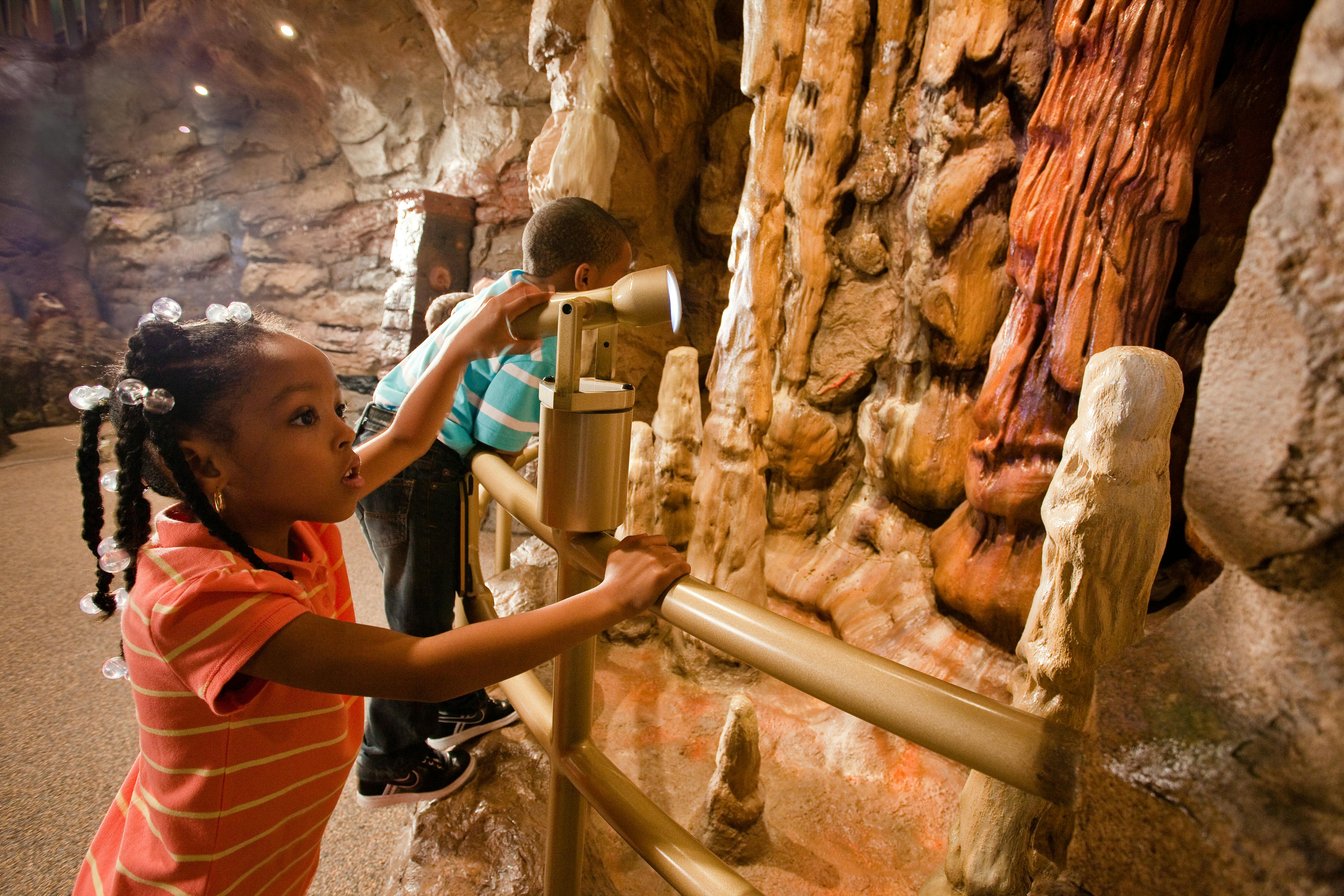 Kinder beobachten mit einem Binokular die Felsformationen in einer Höhle.