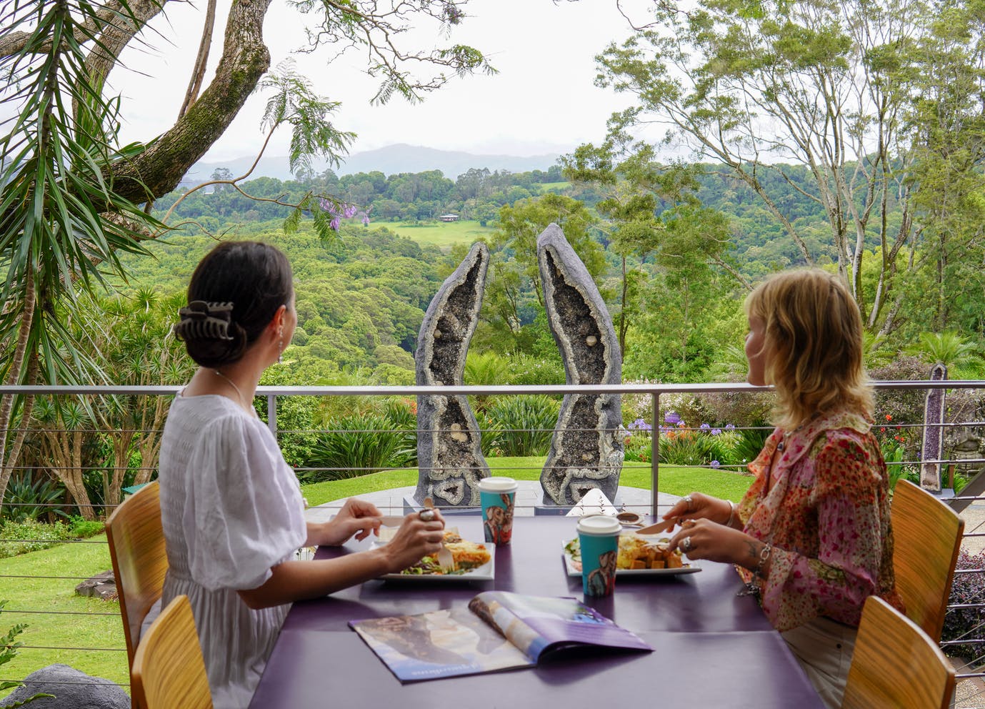 風光明媚な緑の風景と大きなジオードの彫刻を見渡せるテーブルで屋外で食事をする2人。
