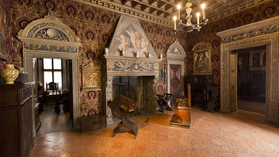 A richly decorated room featuring an ornate fireplace, antique furniture, intricate wallpaper, and classical artwork on the walls.