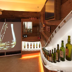 Rum med träinredning, en rad whiskyflaskor på en böjd hylla, en projektion av vätska som hälls i ett glas och "1990" och "2013" väggskyltar.