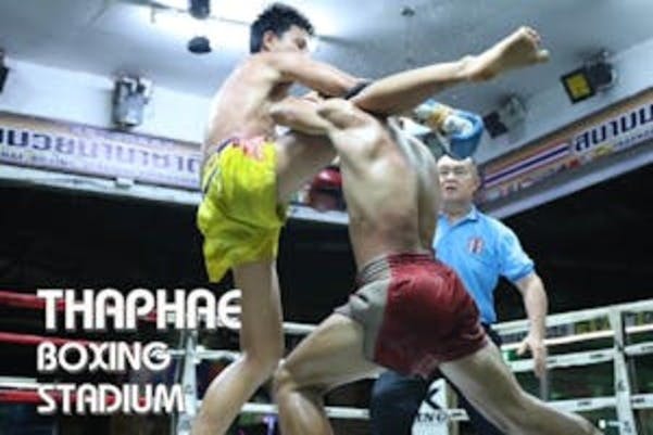 Deux combattants de Muay Thai en action sur un ring de boxe au Thaphae Boxing Stadium, avec un arbitre observant le match.