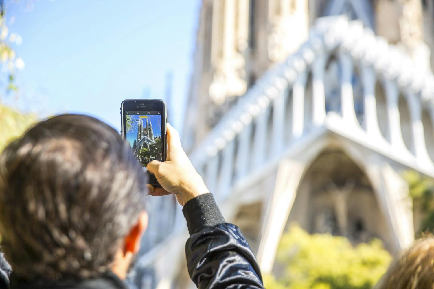 Person taking a photo of a Gothic-style building with a smartphone on a sunny day, focusing on spires and intricate architecture.