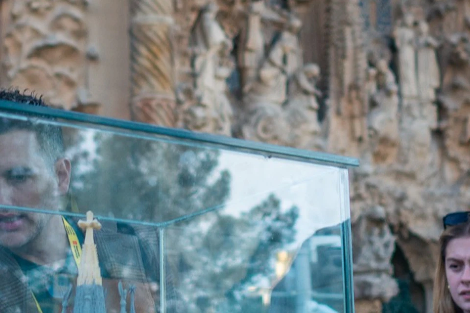 A group of people examining a model of a building displayed in a glass case, with a detailed architectural structure in the background.