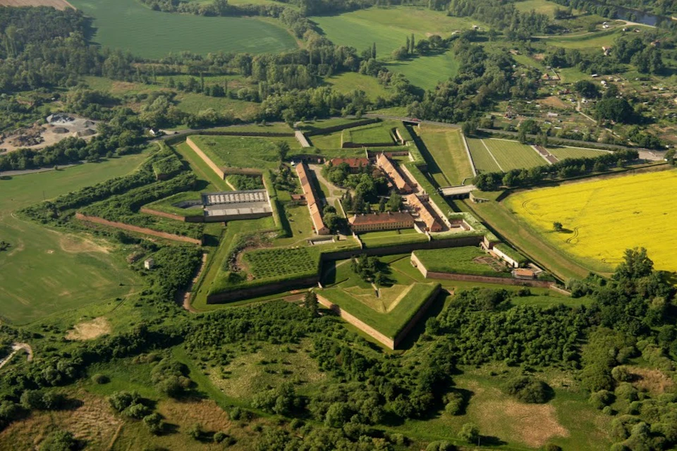 Aerial view of a star-shaped fortress surrounded by greenery and fields, featuring buildings and walls within.