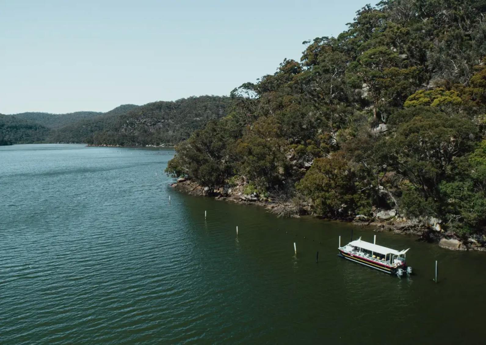 Una piccola barca ancorata vicino a una costa boscosa su un lago calmo con colline sullo sfondo sotto un cielo limpido.