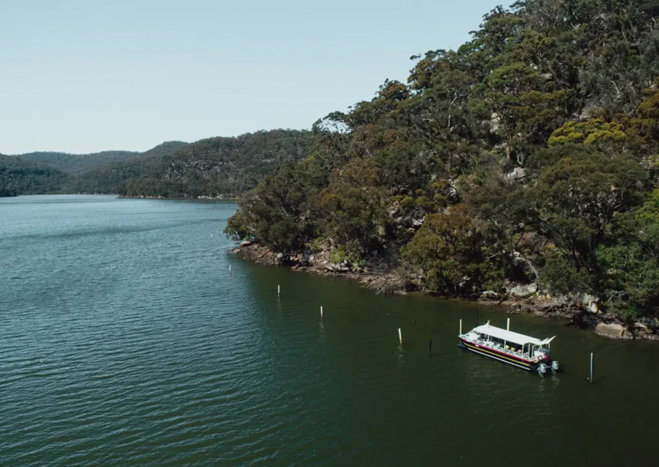 A small boat anchored near a forested shoreline on a calm lake with hills in the background under a clear sky.