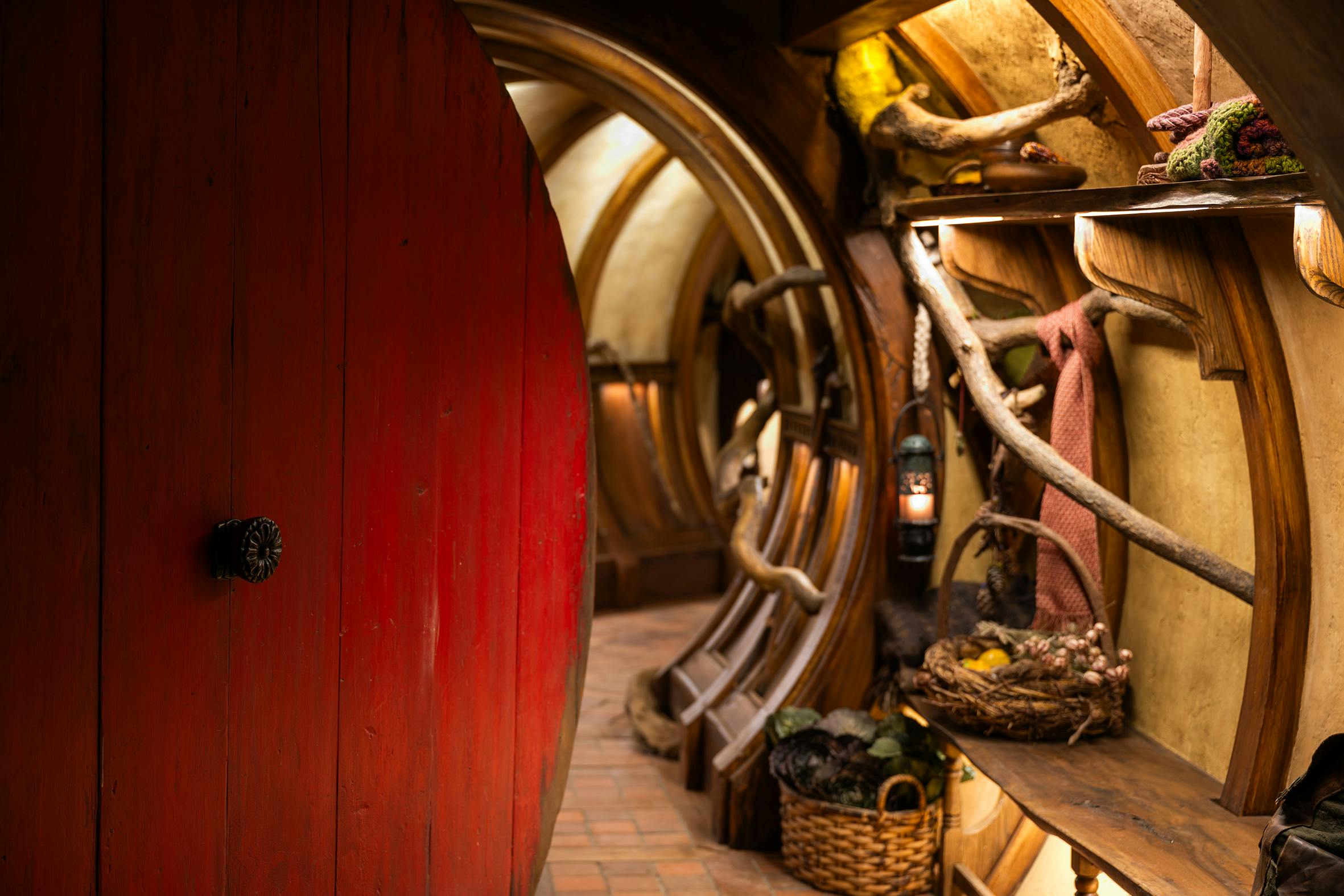 A cozy, rustic hallway with wooden arches, a red door, baskets, lantern, and decorative natural elements.