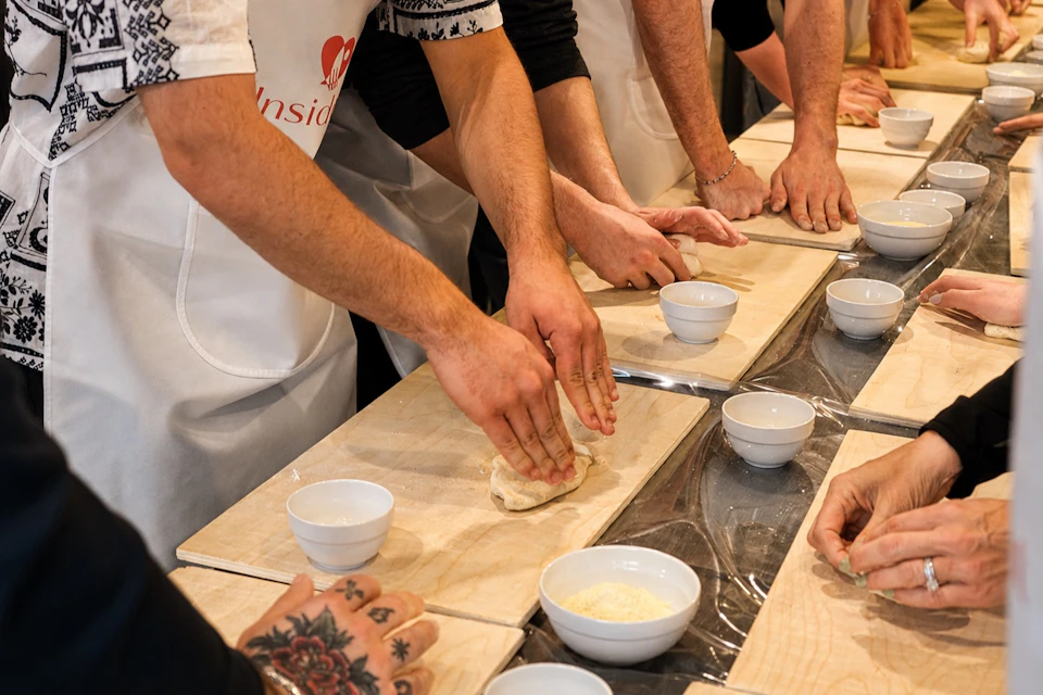 People participating in a cooking class, shaping dough on wooden boards with bowls containing ingredients around.