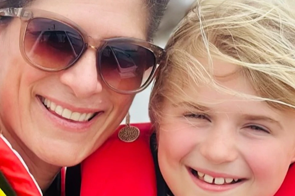 A woman and a child wearing red life jackets smile while sitting on a boat on a sunny day.