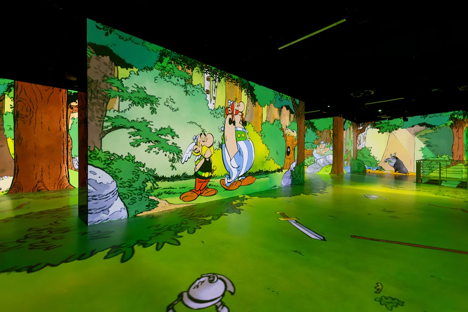 An immersive exhibit featuring Asterix and Obelix in a forest scene, projected onto walls and the floor.