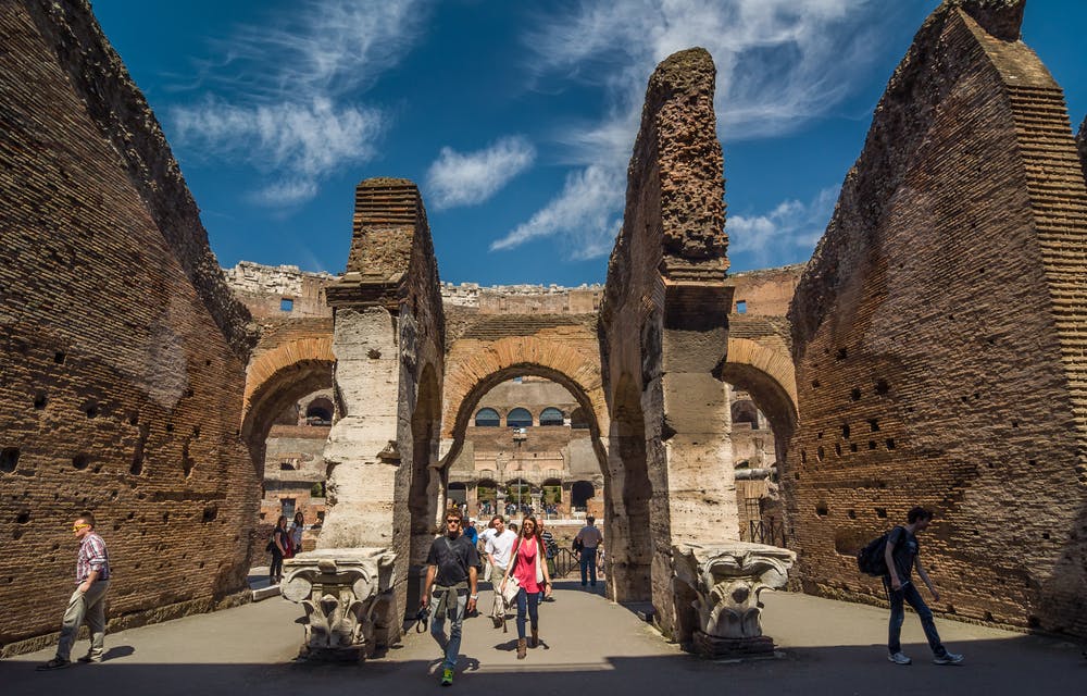 People walking among ancient stone ruins under a blue sky with scattered clouds.