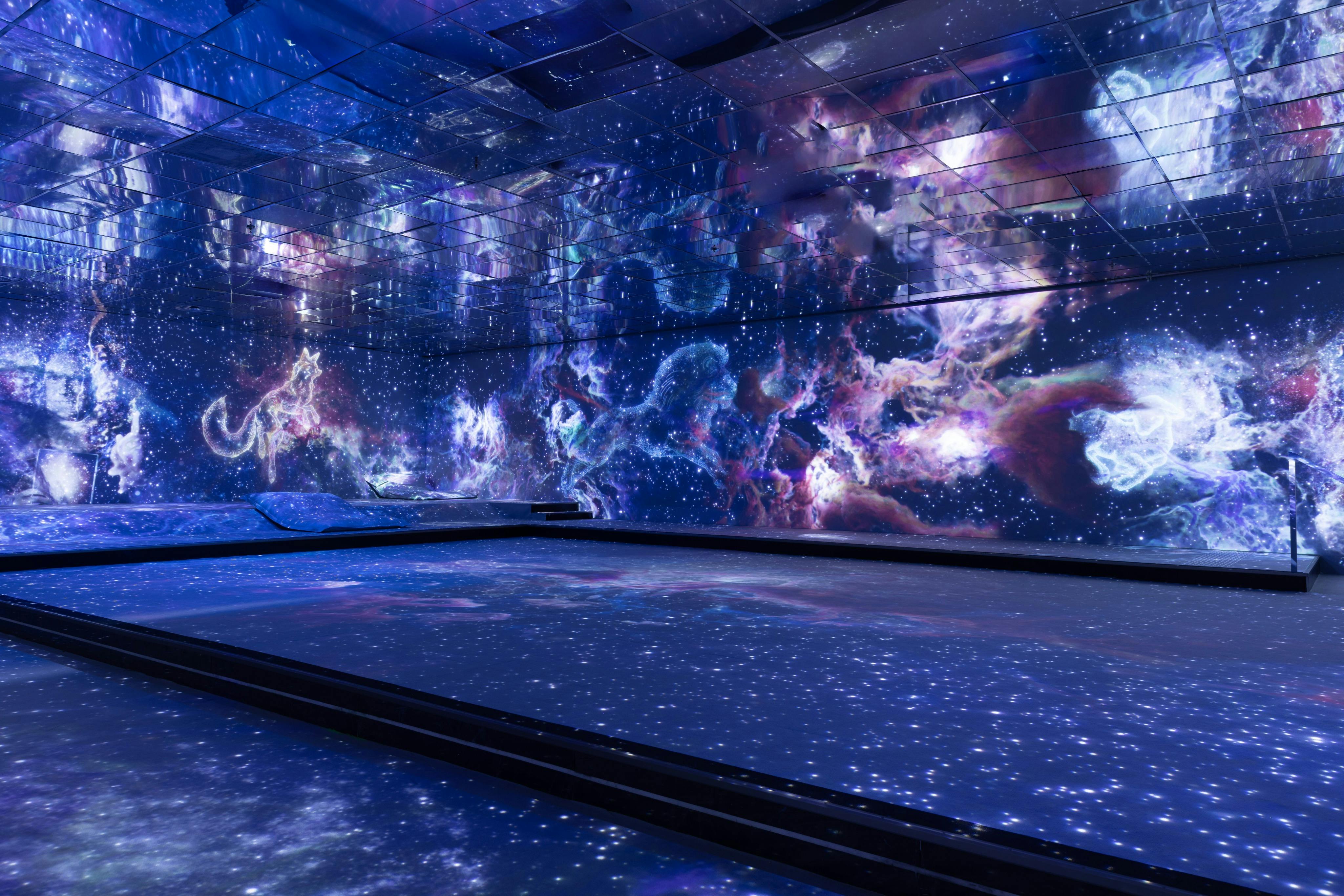Room with walls and floor displaying a vibrant space-themed light show featuring stars, nebulas, and cosmic scenes.