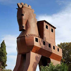 En stor träkopia av en trojansk häst omgiven av träd under en delvis molnig himmel.