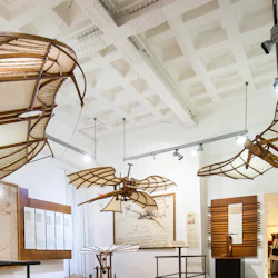 Utställningen visar historiska flygmaskinmodeller och konstverk, inklusive Da Vincis Vitruvian Man, som visas i ett väl upplyst rum. Två personer syns i bakgrunden.
