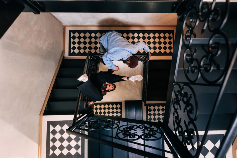 Two people interacting on a decorative staircase with black and white tiled flooring viewed from above.