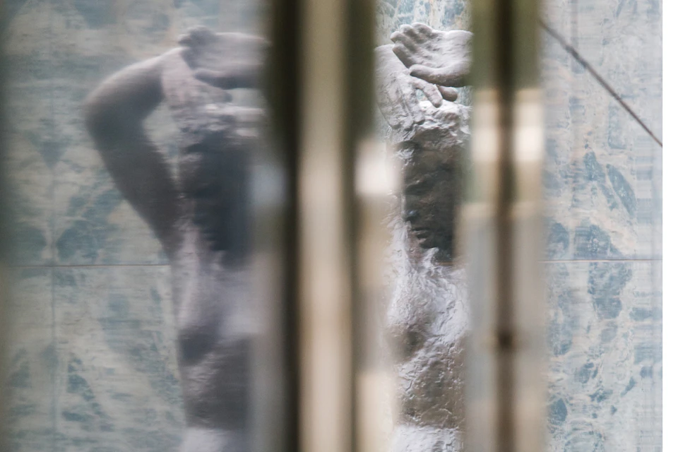 A blurry view of a statue of a person with raised arms, seen through reflective and distorted surfaces.