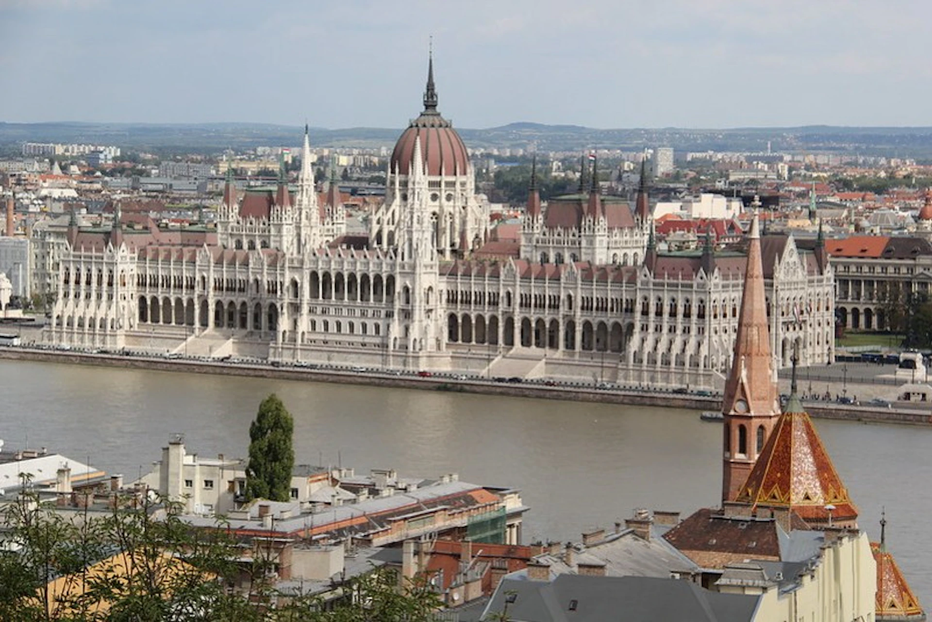 View of the Hungarian Parliament Building on the Danube River with city buildings in the foreground.