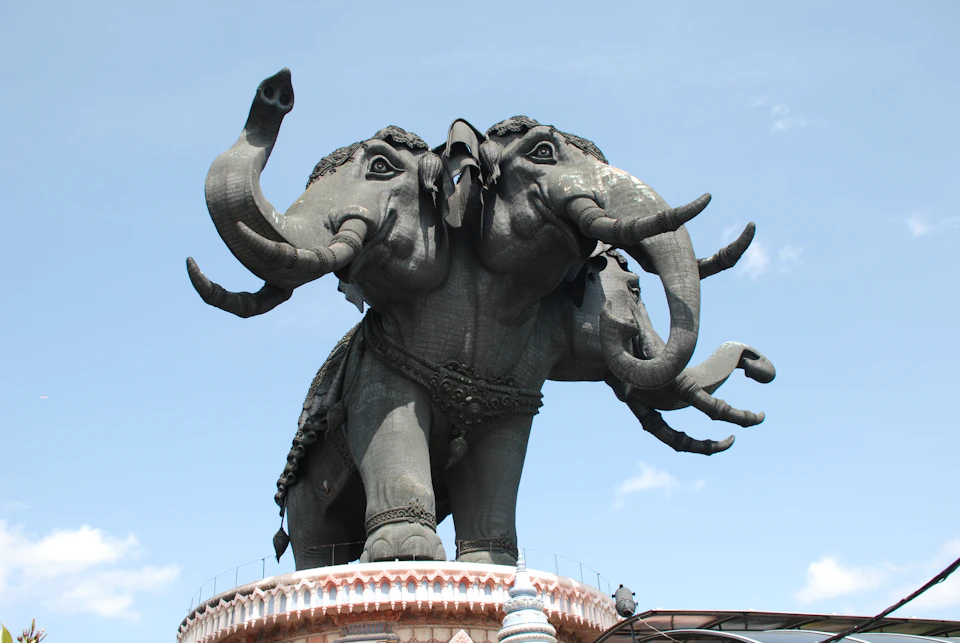 Large statue of a three-headed elephant with ornate details, mounted on a decorative base, under a clear blue sky.