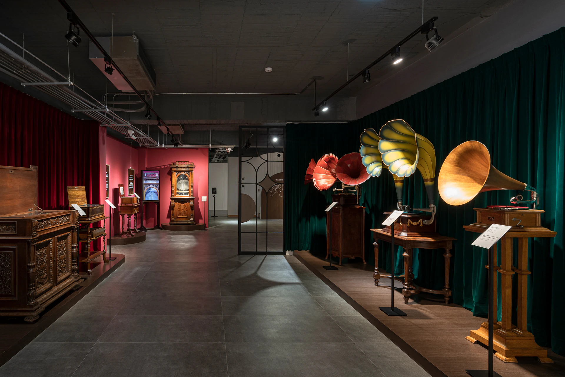 An exhibition room displaying vintage gramophones and antique furniture under dim lighting.