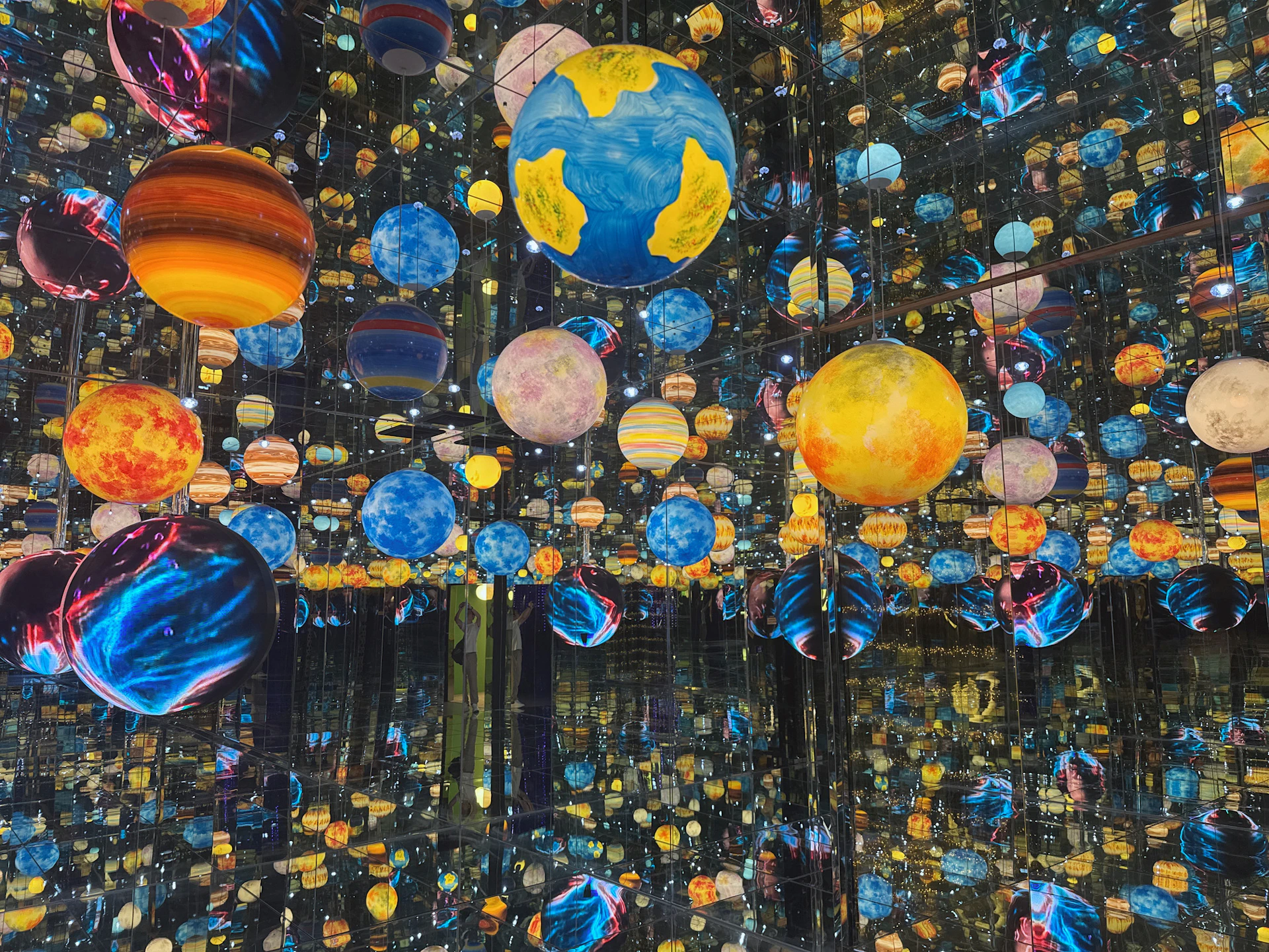 A mirrored room filled with colorful representations of planets and celestial objects, creating an infinite reflection effect.